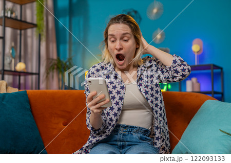 Surprised excited young woman winner holding smartphone reading good news amazed by online game win 122093133