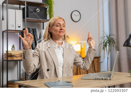Caucasian calm mature businesswoman in suit meditating after using laptop at home office desk Caucasian calm mature businesswoman in suit meditating after using laptop at home office desk 122093307