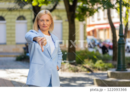 Upset mature Caucasian blonde businesswoman in formal suit looking camera and showing thumb down 122093366
