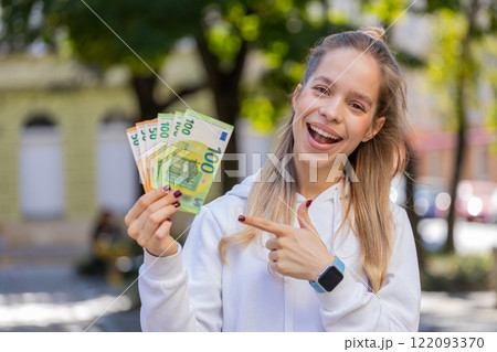 Happy Caucasian young woman girl holding fan of euro showing thumbs up gesture on city street Happy Caucasian young woman girl holding fan of euro showing thumbs up gesture on city street 122093370
