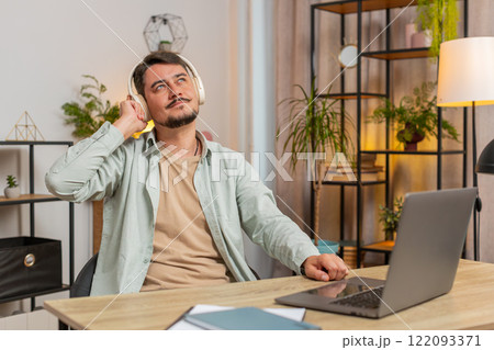 Happy relaxed overjoyed young Caucasian man in wireless headphones listening to music in home room Happy relaxed overjoyed young Caucasian man in wireless headphones listening to music in home room 122093371