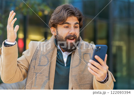 Happy Indian man using smartphone celebrating victory win good message news on downtown city street 122093394