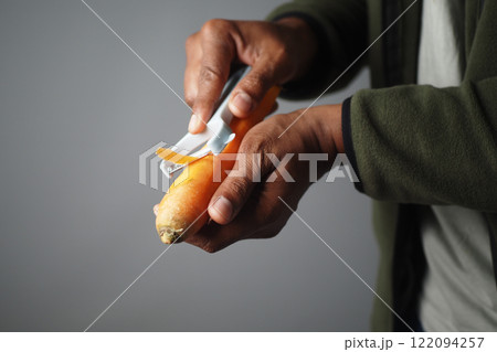 Manual peeling of a fresh carrot using a specialized vegetable peeler tool 122094257