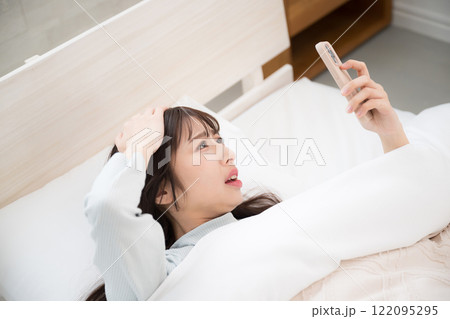 寝坊してベッドでスマホで時間をみる女性 遅刻だ~ 寝坊してベッドでスマホで時間をみる女性 遅刻だ~ 122095295