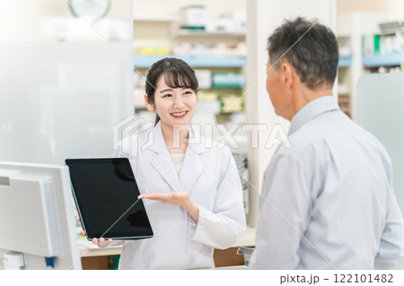 薬局でタブレットPCを使いながら説明する薬剤師・調剤師(レセコン・レセプトコンピュータ) 薬局でタブレットPCを使いながら説明する薬剤師・調剤師(レセコン・レセプトコンピュータ) 122101482