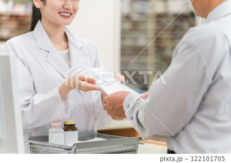 薬局のレジで薬の説明をする薬剤師の女性と高齢者男性 122101705