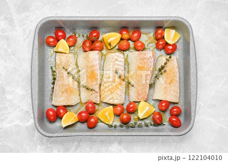Top view of cod fish fillets on a baking tray with tomatoes and lemon wedges 122104010