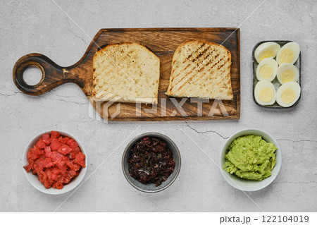 Breakfast spread featuring toast, avocados, caramelised onion, and boiled eggs on a tabletop Breakfast spread featuring toast, avocados, caramelised onion, and boiled eggs on a tabletop 122104019