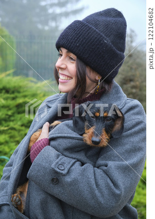 Smiling woman holding her wire-haired dachshund puppy inside her coat Smiling woman holding her wire-haired dachshund puppy inside her coat 122104682