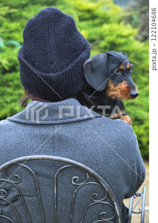 Woman wearing beanie holding her wire-haired dachshund dog in garden Woman wearing beanie holding her wire-haired dachshund dog in garden 122104686