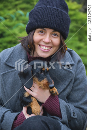 Smiling woman holding her cute wire-haired dachshund puppy outdoors Smiling woman holding her cute wire-haired dachshund puppy outdoors 122104702
