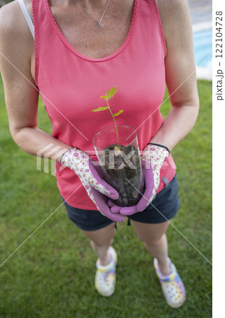Gardener holding small oak sapling in glass jar for planting Gardener holding small oak sapling in glass jar for planting 122104728