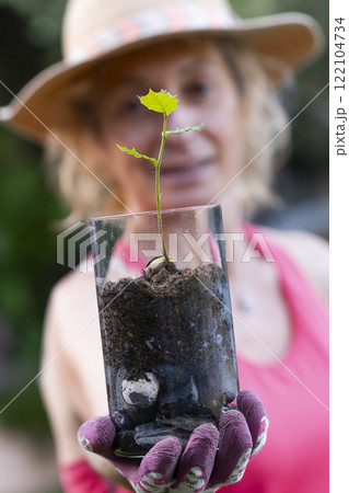 Gardener showing small holly oak sprout growing in glass jar 122104734