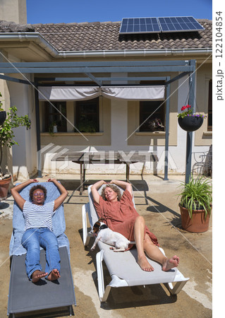 Two women sunbathing in a sunny backyard with a small dog Two women sunbathing in a sunny backyard with a small dog 122104854