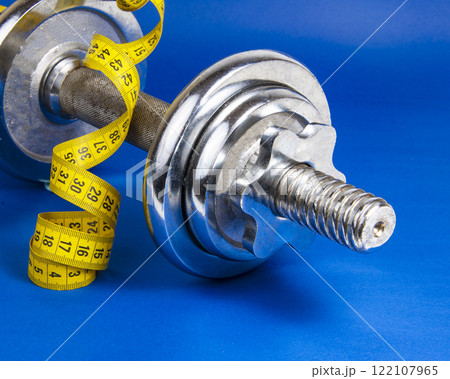Stainless metal dumbbell and yellow tape measure on dark blue background with copyspace for text 122107965