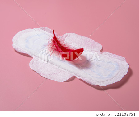 Sanitary napkin pad with red elegant feather lying on pink background 122108751