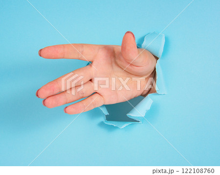 Woman hand in whole of torn blue paper background 122108760