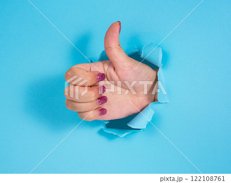 Woman hand in whole of torn blue paper background Woman hand in whole of torn blue paper background 122108761