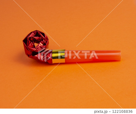 Party foil red horn noisemaker for carnival on the orange background Party foil red horn noisemaker for carnival on the orange background 122108836