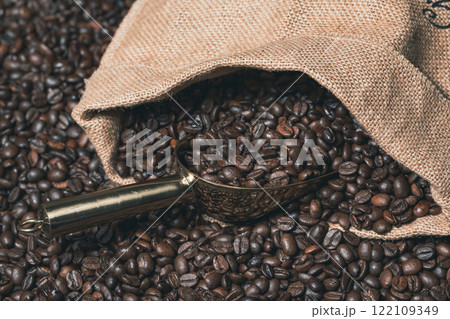 Jute sack full of coffee with a golden coffee scoop on a background of coffee beans Jute sack full of coffee with a golden coffee scoop on a background of coffee beans 122109349