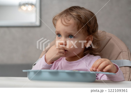 A focused toddler eating at the table during a quiet moment at home 122109361