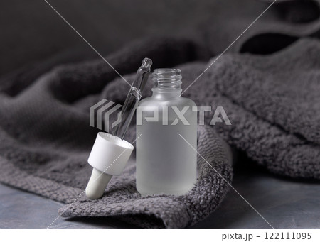 Pipette set on opened clear glass dropper bottle near dark grey bath towel closeup, cosmetic mockup Pipette set on opened clear glass dropper bottle near dark grey bath towel closeup, cosmetic mockup 122111095