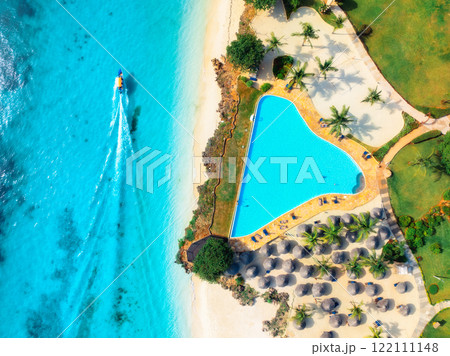 Aerial view of pool, sandy beach, umbrellas, boat, blue sea 122111148