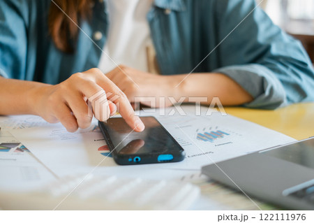 Close-up of a person using a smartphone to review financial documents and charts, highlighting modern business analysis. 122111976