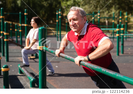 Elderly man doing exercises on a horizontal bar at an outdoor sports ground Elderly man doing exercises on a horizontal bar at an outdoor sports ground 122114236