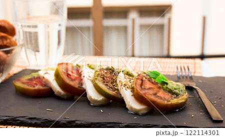 Caprese salad with mozzarella, black tomatoes and pesto on black stone plate Caprese salad with mozzarella, black tomatoes and pesto on black stone plate 122114301