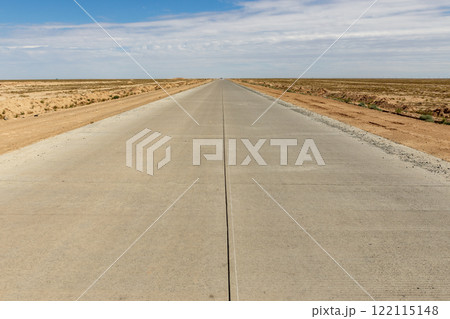 Long concrete road stretches through the vast landscape of Karakalpakstan in Uzbekistan Long concrete road stretches through the vast landscape of Karakalpakstan in Uzbekistan 122115148
