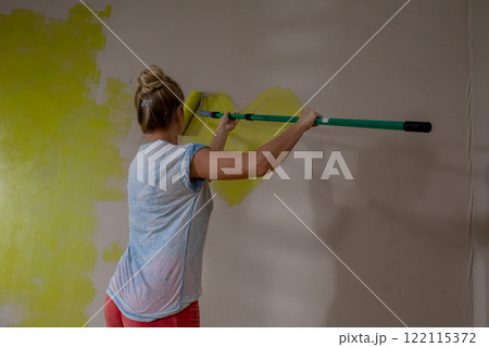 A Person is Painting a Wall Using a Roller That is Coated in a Bright Yellow Color 122115372
