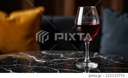 Elegant glass of red wine on a marble table with plush pillows in a cozy interior setting Elegant glass of red wine on a marble table with plush pillows in a cozy interior setting 122115755