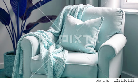 Cosy armchair with thick knitted plaid in light blue colour and cushion. Home decor in a romantic style. Cosy armchair with thick knitted plaid in light blue colour and cushion. Home decor in a romantic style. 122116113
