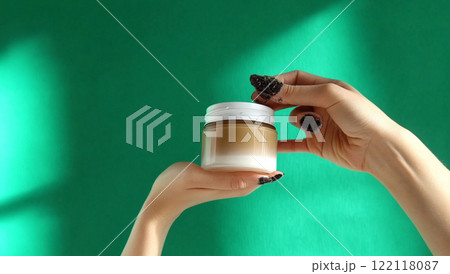 Beautician holding cosmetic cream jar on green background Beautician holding cosmetic cream jar on green background 122118087