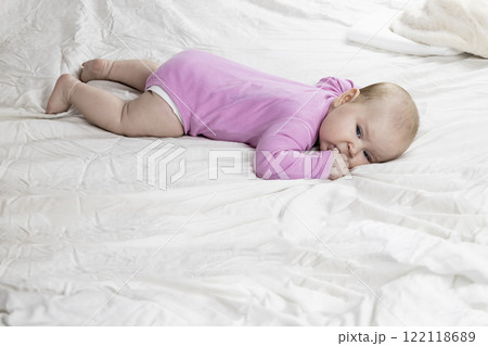Cute and beautiful 4-month-old baby girl laying on bed. Infant in pink bodysuit on bed against white background. 122118689
