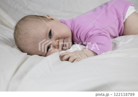 Cute and beautiful 4-month-old baby girl laying on bed and look at the camera. Infant in pink bodysuit on bed against white background. Cute and beautiful 4-month-old baby girl laying on bed and look at the camera. Infant in pink bodysuit on bed against white background. 122118789