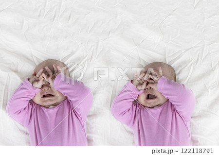 Set of two photos of 4-month-old baby girl laying on bed and crying. Infant in pink clothes wants to sleep and rubs eyes Set of two photos of 4-month-old baby girl laying on bed and crying. Infant in pink clothes wants to sleep and rubs eyes 122118791