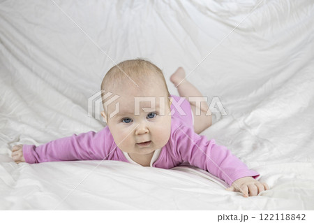 Cute and beautiful 4-month-old baby girl laying on bed and look at the camera. Infant in pink bodysuit on bed against white background. Cute and beautiful 4-month-old baby girl laying on bed and look at the camera. Infant in pink bodysuit on bed against white background. 122118842
