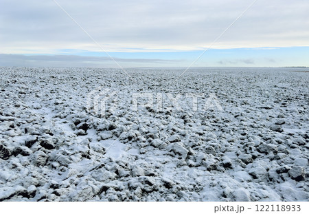A field of black soil plowed for the winter, covered with snow against the background of a blue winter sky A field of black soil plowed for the winter, covered with snow against the background of a blue winter sky 122118933
