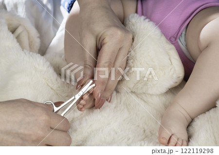 Mom trims baby's nails with baby scissors. Close up photo of mother's hands holding feet of the infant and nail scissors. Mom trims baby's nails with baby scissors. Close up photo of mother's hands holding feet of the infant and nail scissors. 122119298