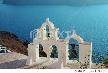 Ancient bell tower with old bells of a Christian church against the background of the blue sea. Ancient bell tower with old bells of a Christian church against the background of the blue sea. 122119363