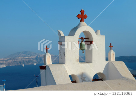 An ancient bell tower with old bells of a Christian church in the Greek style against the background of the blue sea. Caldera of Santorini island. An ancient bell tower with old bells of a Christian church in the Greek style against the background of the blue sea. Caldera of Santorini island. 122119365