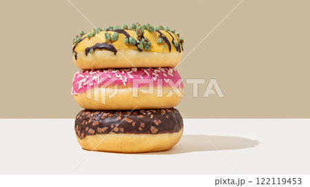Stack of glazed donuts with different toppings on beige and white minimalistic background close up. 122119453