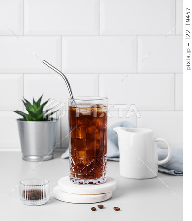 Cold brew coffee in a glass with ice and straw on a light table against a white brick background 122119457