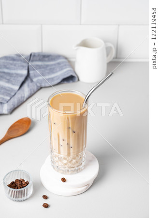 Cold latte coffee in a tall glass with milk and straw on a light table on a white brick background Cold latte coffee in a tall glass with milk and straw on a light table on a white brick background 122119458