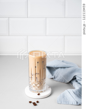 Cold latte coffee in a tall glass with alternative milk on a light table on a white brick background Cold latte coffee in a tall glass with alternative milk on a light table on a white brick background 122119459