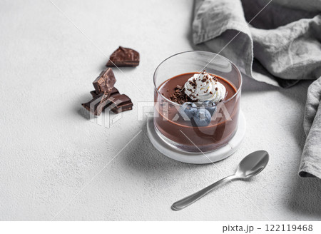 Chocolate pudding in a glass with whipped cream and fresh blueberry on a light background 122119468