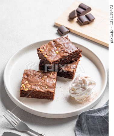 Chocolate brownie with nuts cut into pieces on a plate with whipped cream on a light background 122119472