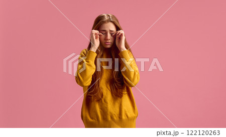 Caucasian red-hair woman in her 20s keeping her eyes closed, suffering from seasonal allergy and allergy on products on pink studio background 122120263